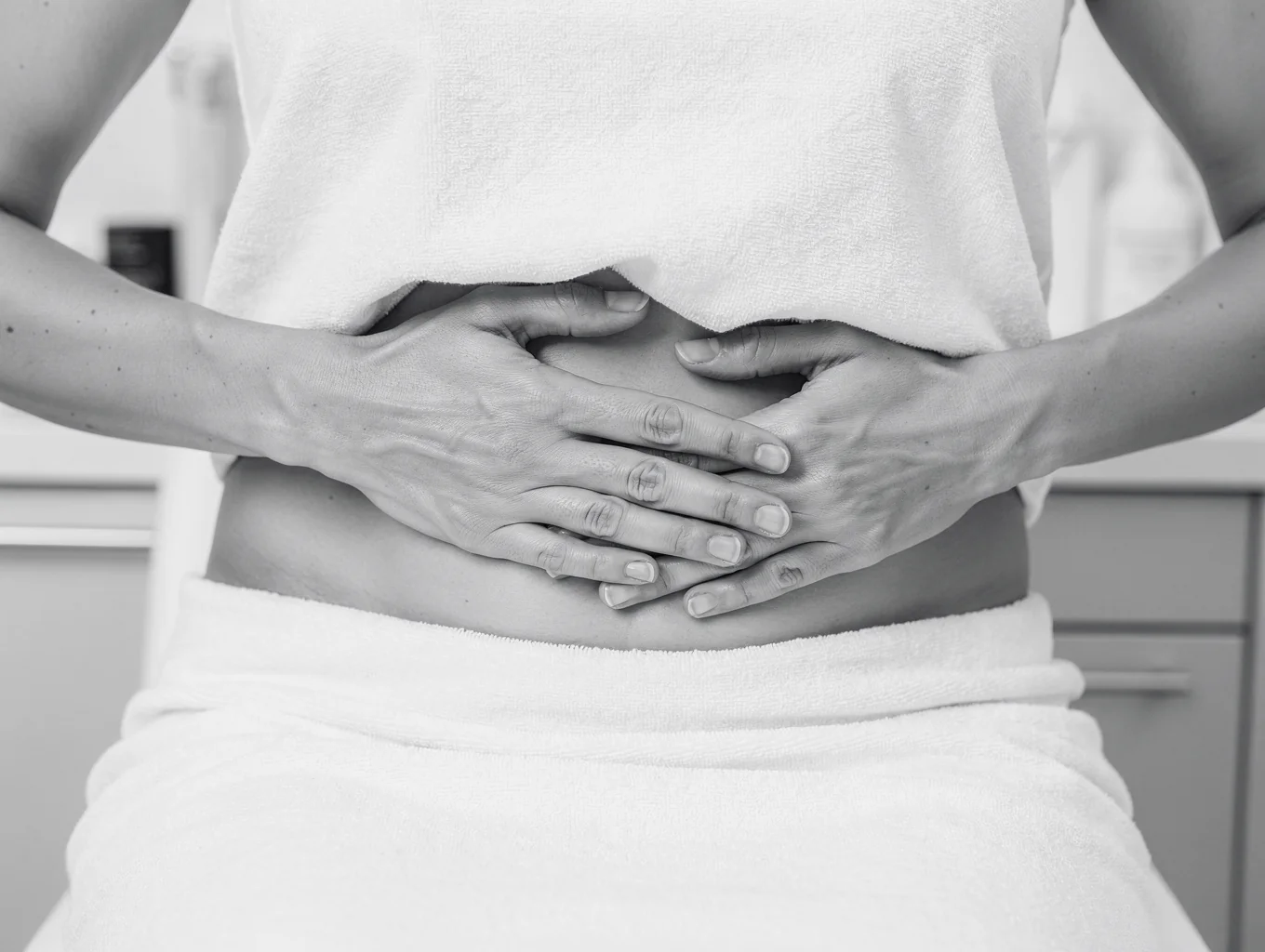 Practitioner performing gentle manual lymphatic drainage massage on a client's draped abdomen